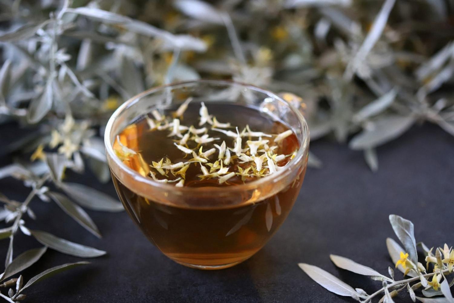 Glass cup of golden tea infused with dried flowers, showing clean water clarity